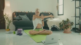 Woman doing stretching on the floor at home in front of her laptop, online yoga class