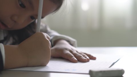closeup hand of asian child student or kid girl writing and enjoy doing homework on book or learning and training write on paper with eraser on table by learn from home and back to school study online