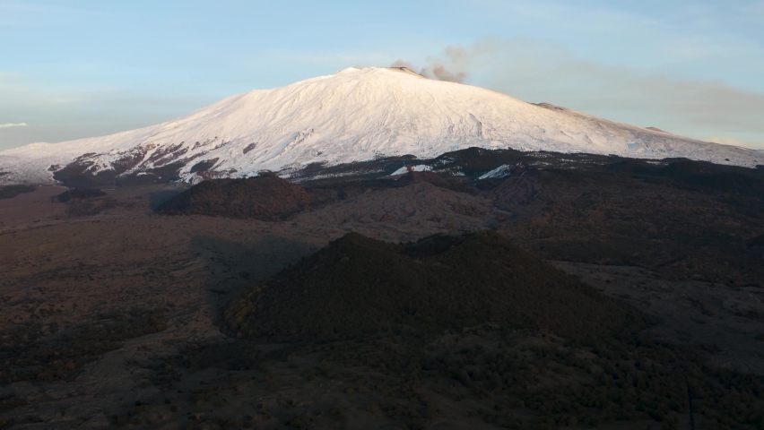 The snow-capped Etna volcano with lava flows and craters at the base.	