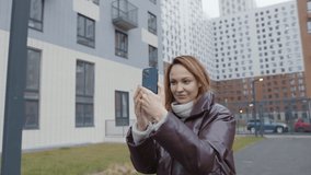 Beautiful woman takes pictures on phone of building. Action. Woman shoots and takes photo on phone on background of residential high-rise buildings