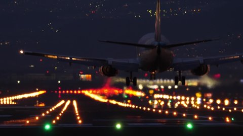 OSAKA, JAPAN - APRIL 10, 2018: Commercial jet liner landing at airport in night time, telephoto view, lengthwise perspective of runway. Plane move down and forward, touch down land and roll ahead