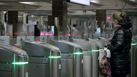 RUSSIA, MOSCOW, 27 FEB 2021: woman uses electronic touch card to pass through submay turnstile after green light. metro wicket control panel, paying for entrance. title says ONLY IN MASK AND GLOVES