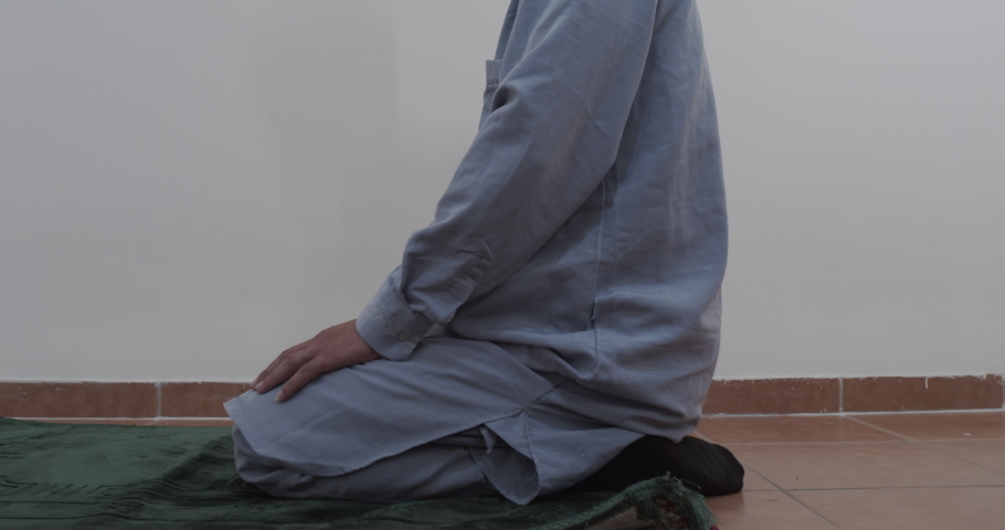 Muslim man bows down in prayer panning right to left in slow motion, ground angle