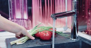 Women's hands take an onion from the sink and begin to thoroughly wash it under water in the kitchen. She tries to do it very carefully. The onion should be very clean.