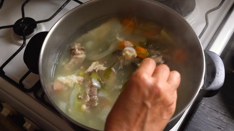 Cooking And Stirring Nutritious Chicken Soup With Carrots And Leafy Vegetables In A Pot. close up