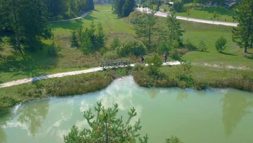 Drone view of two cyclists biking along the lakeside.