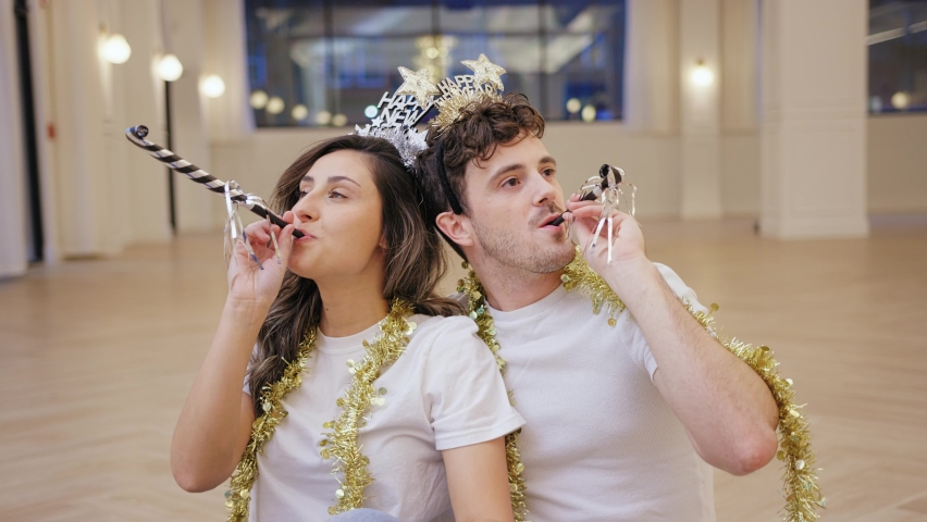 Man and woman blow noise makers and smile with new year crowns and gold tinsel