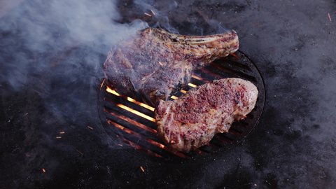 Rib eye steaks with spices on a barbecue grill grate with a blazing fire. Slow camera rotation. 4K slow motion.
