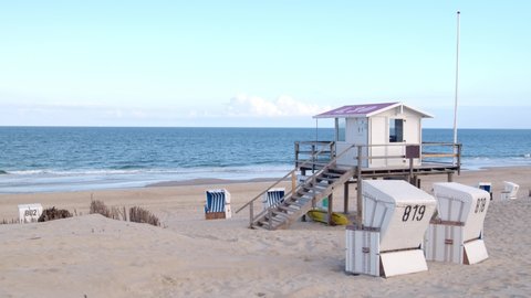 Beautiful beach on the German island of Sylt with white sand, blue sky, a lifeguard station and two beach chairs.