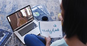 African american woman holding a document having a video call with female colleague on laptop. business, professionalism and technology concept