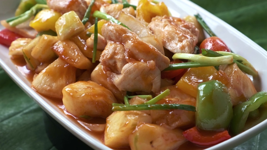 sweet and sour chicken with vegetables in a white dish spinning around