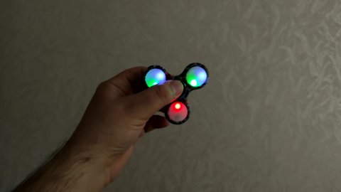 Rotating spinner with LED light in a hand of man. Fidgeting spinner, hand spinner rotating. Toy to relax known spinner.