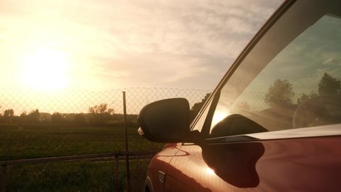 Red car in beautiful summer sunset scenery behind wire fence