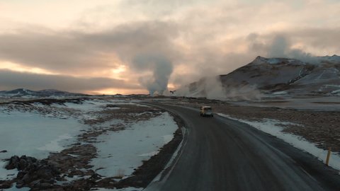 Aerial View of Car on Countryside Road in Iceland Moving Toward Vapors of Geyser Geothermal Hot Springs Under Volcanic Hills, Cinematic Drone Shot