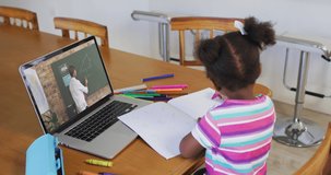 African american girl doing homework while having a video call with male teacher on laptop at home. distance learning and online education concept