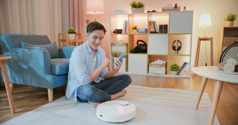 asian man control people-oriented robot vacuum cleaner by smartphone and he feel interesting