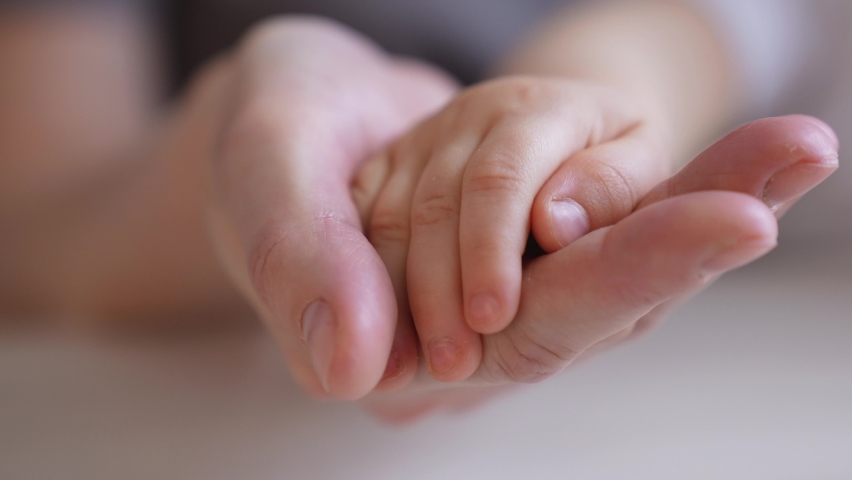 Mom holds the hand of a newborn. close-up baby hand. hospital caring happy family medicine concept. baby newborn holding mom hand close-up. mom takes care indoor of the baby in the hospital | Shutterstock HD Video #1073074331
