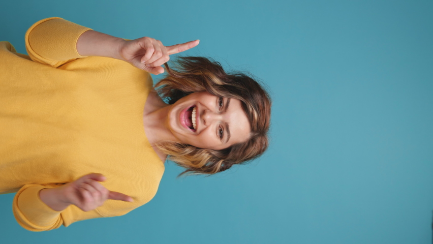 Vertical video Happy young woman blogger close up dancing hands up on copy space for advertising moving rhythmically to music curly hair share video to social media, stories on blue background banner. Royalty-Free Stock Footage #1073075105