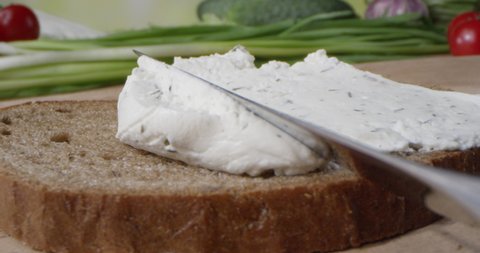 Creamy Textured Paste with Dill is Spreading on the Toast of Bread with Butter Knife with Vegetables on the Background
