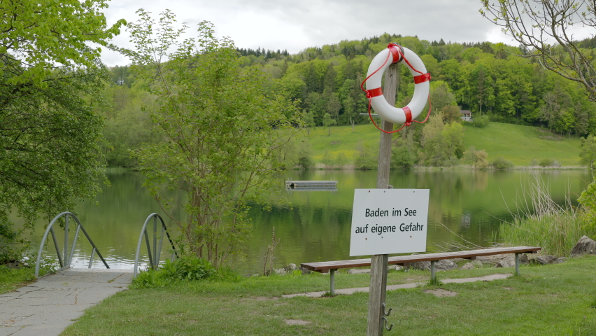 lake outdoor pool with swimming platform in green landscape with notice sign in german, german text translation: swim in the lake at your own risk at the lake, focus strong on the text panel