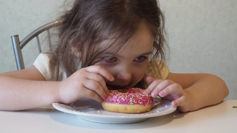 Little happy cute girl is eating donut. child is having fun with donut. Tasty food for kids. Funny time at home with sweet food. Bright kid. Donut with chocolate.