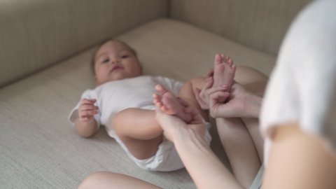 woman mother helping baby infant relieve gassy pain from gas in tummy. baby massage. Mom doing gymnastics with kid. Mommy massaging cute baby girl. Moving baby legs to help relieve constipation gas.