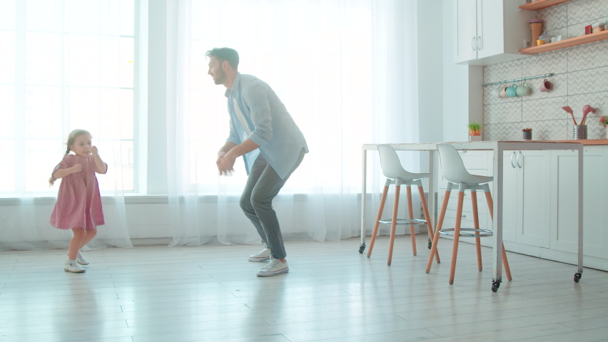 Dancing young father and little preschool girl in the living room. Cute princess and her daddy in the room