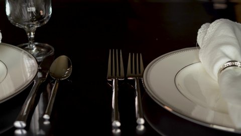 4K close up slide by clip of beautiful set table with silver and white china, cutlery, lace linen napkins and water glasses. 