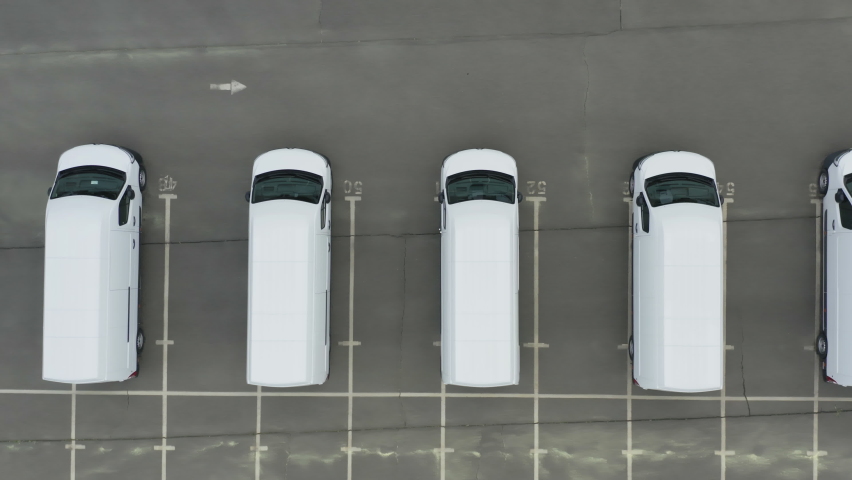 Minibuses (station wagon or short bus) stand on the dealership or customs terminal.  Aerial top down view of a rows of a new commercial vehicles