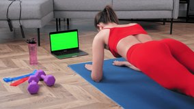 Mockup chroma key monitor laptop: Strong fitness woman in sportswear doing plank exercise workout on yoga mat looking green screen computer display. Fit girl training online video call webcam at home