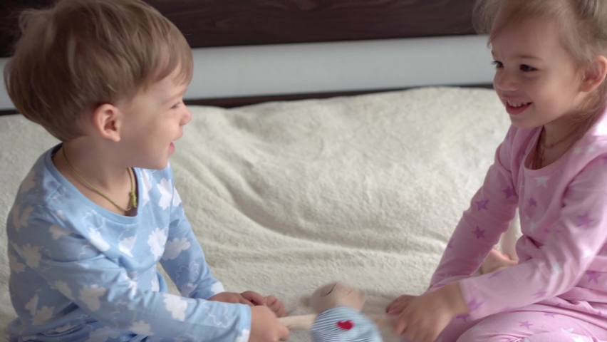 2 smiling preschool toddler children boy and girl fighting over a toy in blue pink pajamas on bed. little baby twins have fun, happy kids on quarantine at home. Friendship, family, education concept Royalty-Free Stock Footage #1073115329