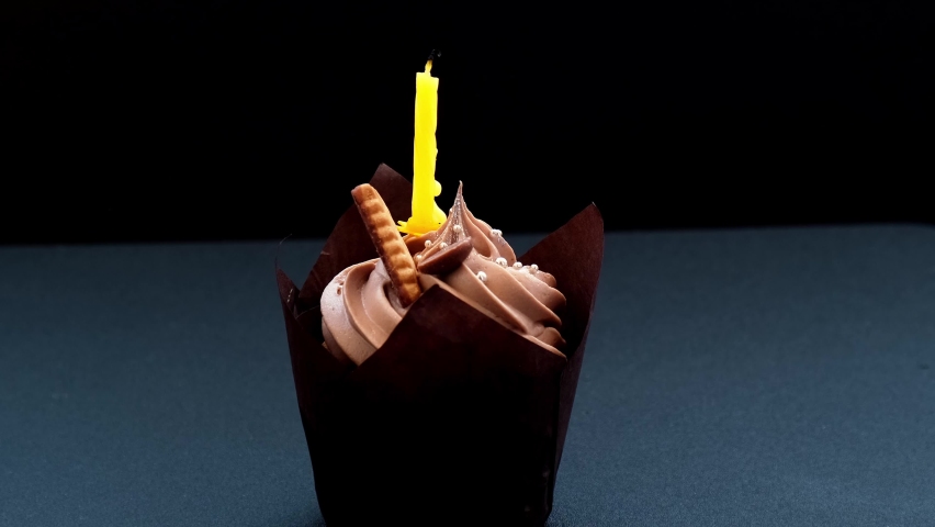 Female hands making Delicious chocolate cupcakes with cream on dark background. Homemade Chocolate muffin. Birthday cake with candle burning. Flame. Blowing out.