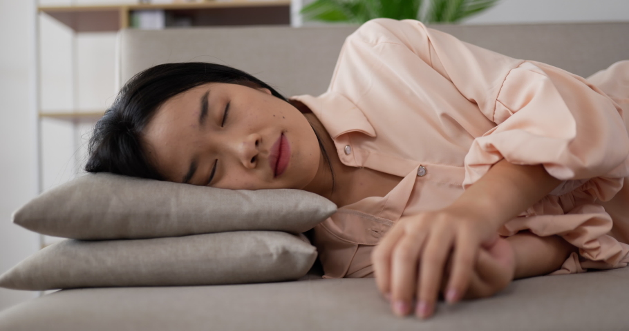 Handheld of Asian woman leaning down on a pillow with exhaustion. Exhausted or bored sleepy woman falls down on sofa. Asian tired teenage girl sleeping on couch. Relaxing and sleeping concept. | Shutterstock HD Video #1073124047