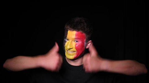 Happy football fan celebrate victory of his favourite team Belgium. Young man with face painted in national colours of Belgian Flag. Portrait of young man supports his national team at home