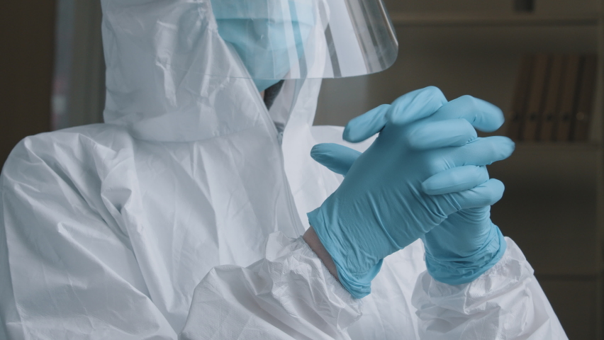 Unrecognizable woman doctor medical worker wears special protective suit uniform puts on rubber latex blue gloves preparing to examine sick patient working in hospital clinic during covid-19 pandemic - Powered by Shutterstock - Get 15% off with code: PIKWIZARD15