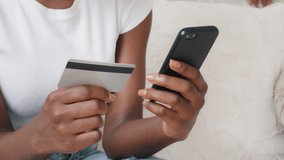 Close-up young African American female shopper holding smartphone and credit card in hands using instant easy mobile payments making purchase in online store receiving cashback. E-banking service - Powered by Shutterstock - Get 15% off with code: PIKWIZARD15