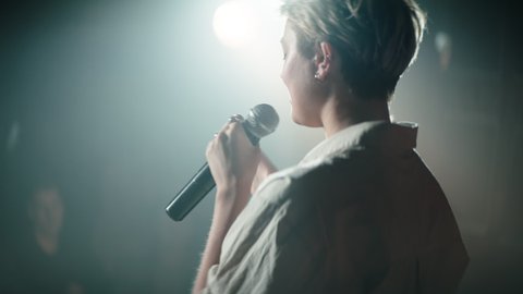 HANDHELD CU Portrait of young Caucasian female comedian entering stage and performing her stand-up monologue in a crowded venue. Shot with ARRI Alexa Mini LF with 2x anamorphic lens
