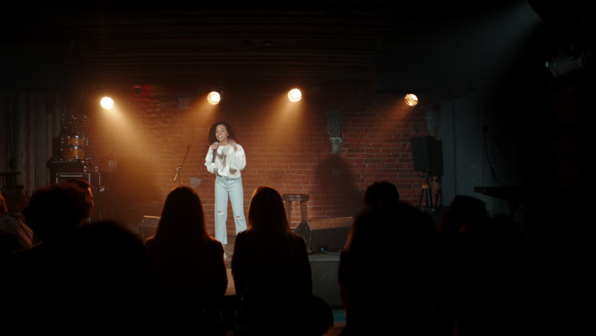 DOLLY Black African American young female comedian finishing her stand-up monologue and leaving stage of a small venue. Shot with ARRI Alexa Mini LF with 2x anamorphic lens Royalty-Free Stock Footage #1073129738