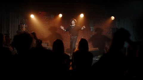 HANDHELD Young Caucasian male comedian entering stage and greeting audience, performing his stand-up monologue inside a small venue. Shot with ARRI Alexa Mini LF with 2x anamorphic lens