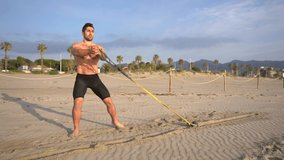 muscular athlete training functional and core exercises performs dragging on the beach with weight at sunrise