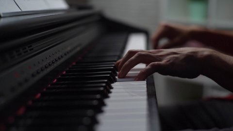 Hand held shot of unrecognizable musician man playing on synthesize at home studio during lesson. Close-up hands of male playing on digital piano in living room. Tracking shot in slow motion.