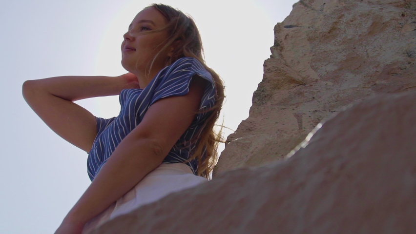 Close Up Charming blonde woman with fluttering hair among rocks in sunshine. Stylishly Dressed Blonde Woman Having Fun Outdoor California 4K