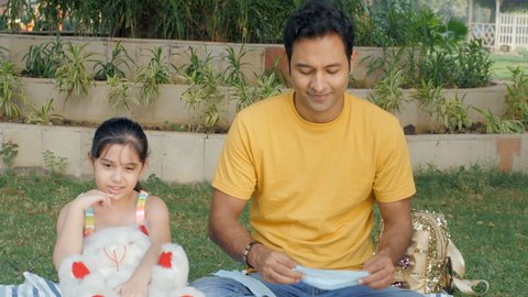 Young father and his little daughter wearing a medical mask - COVID-19 spread . Caring Indian dad helping his little girl-child to wear her mask properly - health and medical