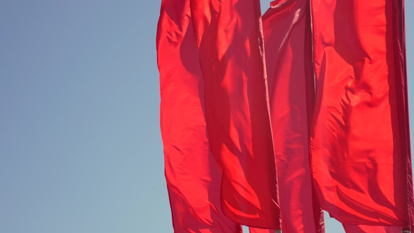 red flags fluttering in the wind a weave against the sky. danger victory communism concept. fabric red flag textile weave in the wind. many red flags on a blue sky background alert