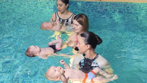 Several young children under the age of one learn to swim with their mothers in a pool with an instructor.Swimming of newborns. Swimming pool in the hotel. Aqua treatments. Chlorine-free swimming pool