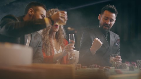 Two bearded men and young woman are winning and rejoice in victory at the casino. Entertainment industry and luxury lifestyle. Concept of casino gambling and poker.