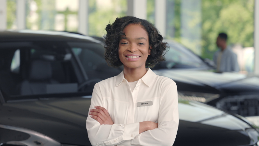 Smiling auto salon manager in formal uniform posing at favorite work with crossed hands. African confident car dealer providing professional service for customers. Portrait. Royalty-Free Stock Footage #1073165483