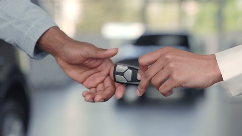 Car manager giving keys to customer at salon. Man and woman shaking hands for making deal. Close up of hands, blur background. Concept of car selling.