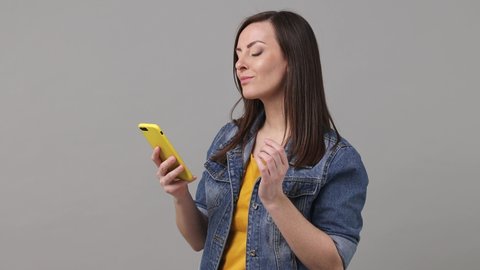 Woman 20s years old in denim jacket yellow t-shirt hold use mobile cell phone swipe chatting send sms doing online shopping order delivery to home booking tour isolated on grey color background studio