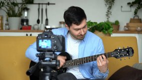 Smiling blogger shoots video on camera playing electric guitar at home. Music video blogging. Video tutorial, online music training.